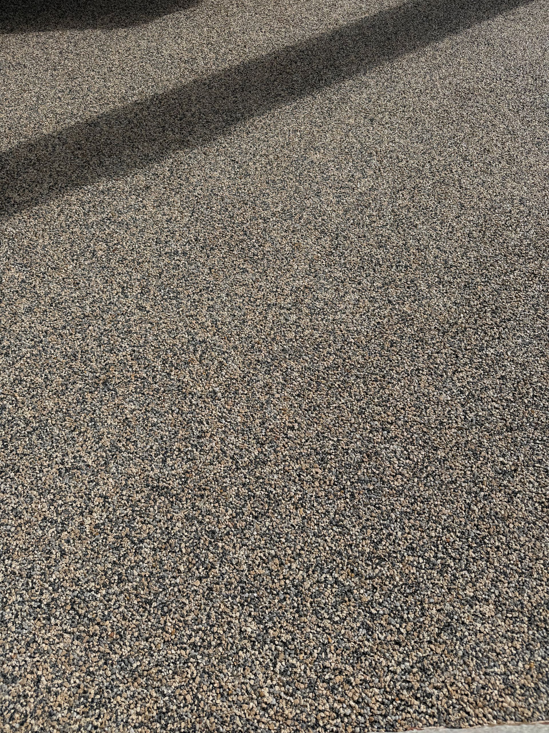 Close-up of speckled gray pavement with a dark diagonal shadow across the top left.