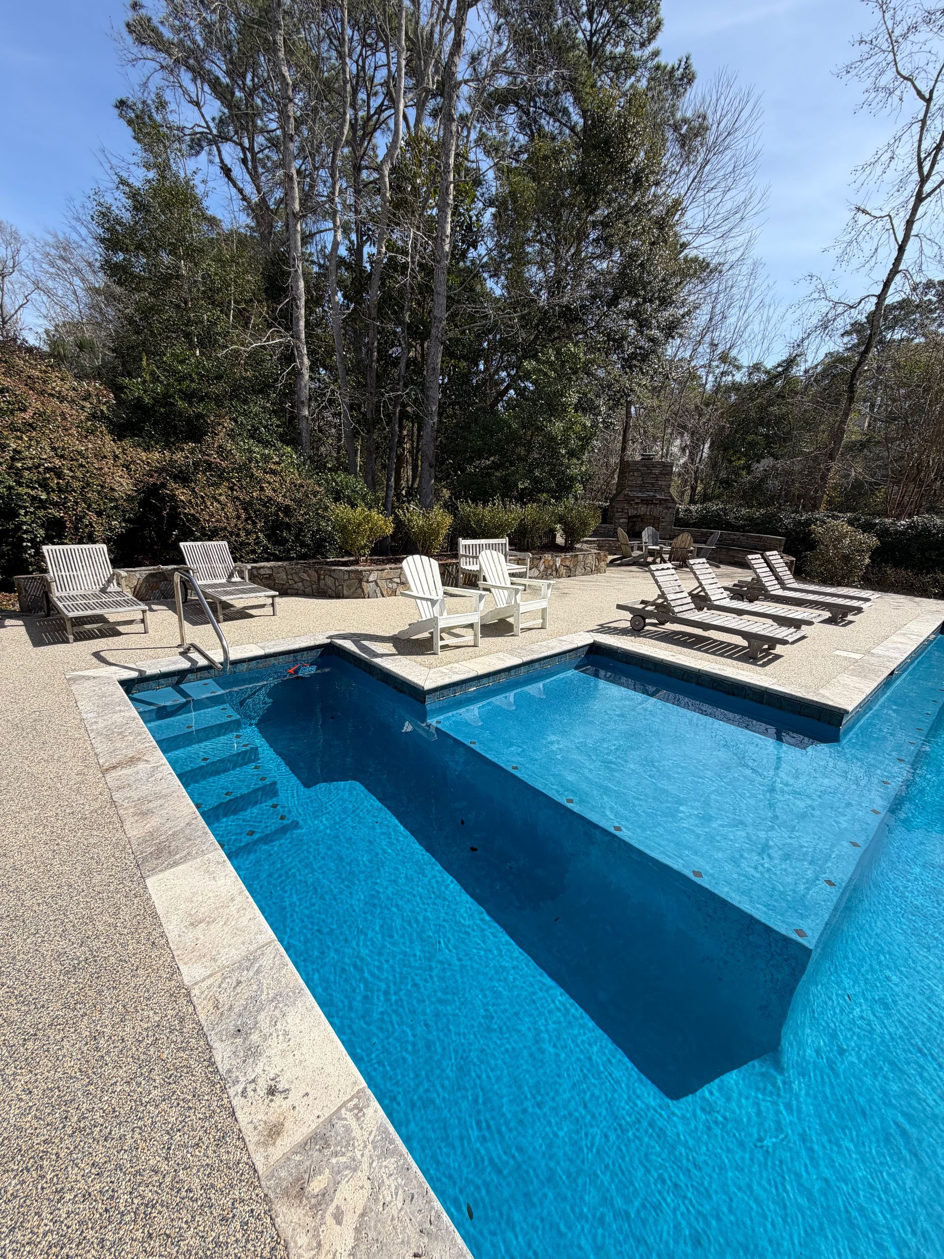 Backyard swimming pool with blue water, stone deck, and lounge chairs under trees