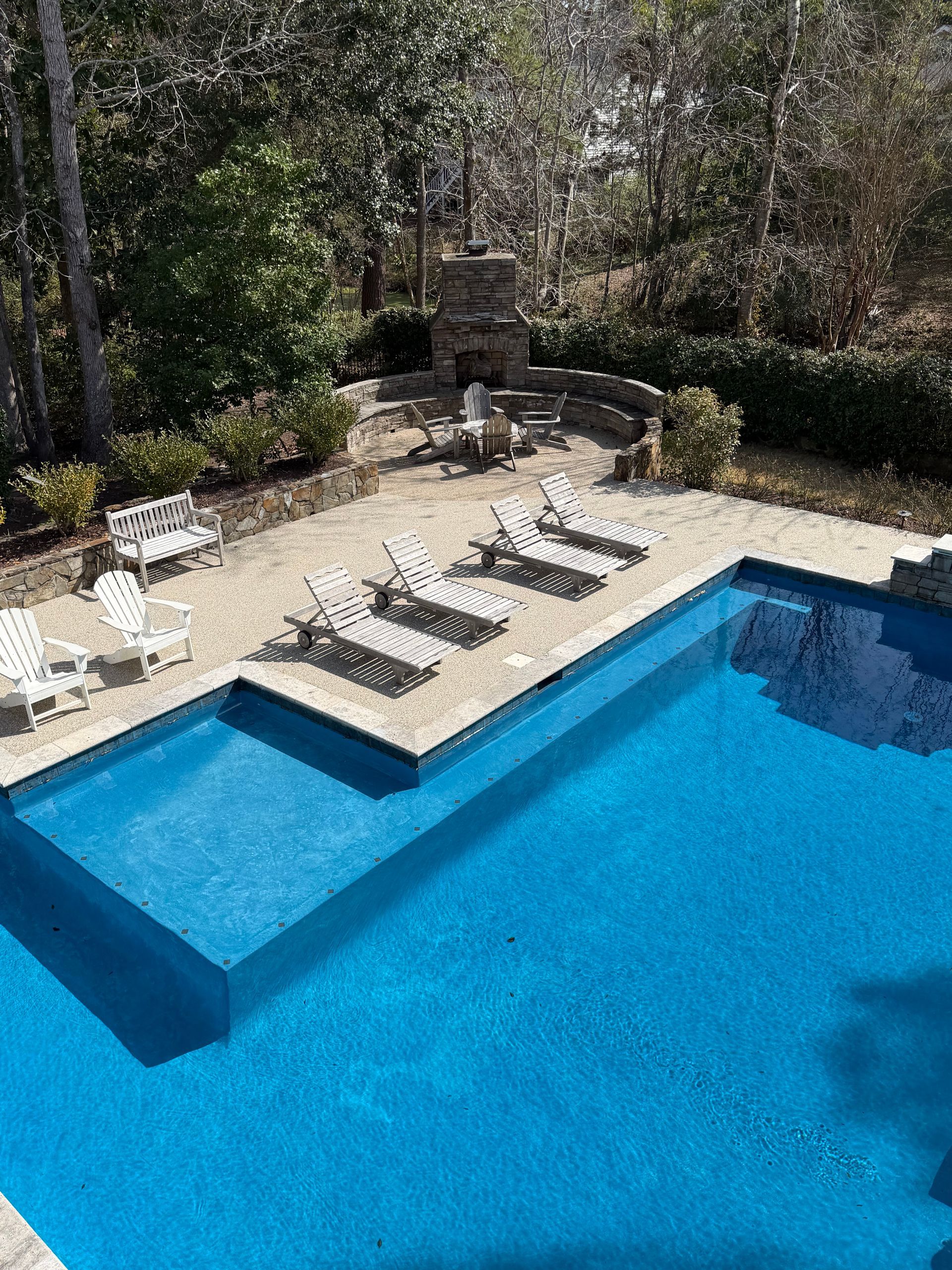 Backyard swimming pool with blue water, stone deck, and lounge chairs by trees