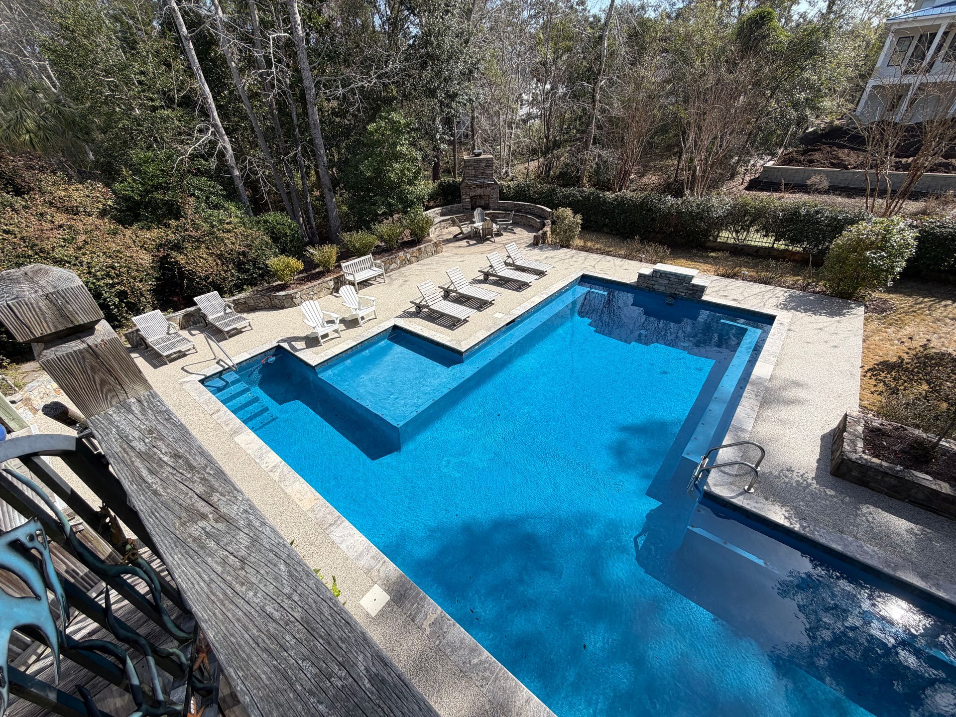 Backyard swimming pool with blue water, stone deck, and lounge chairs in a sunny garden