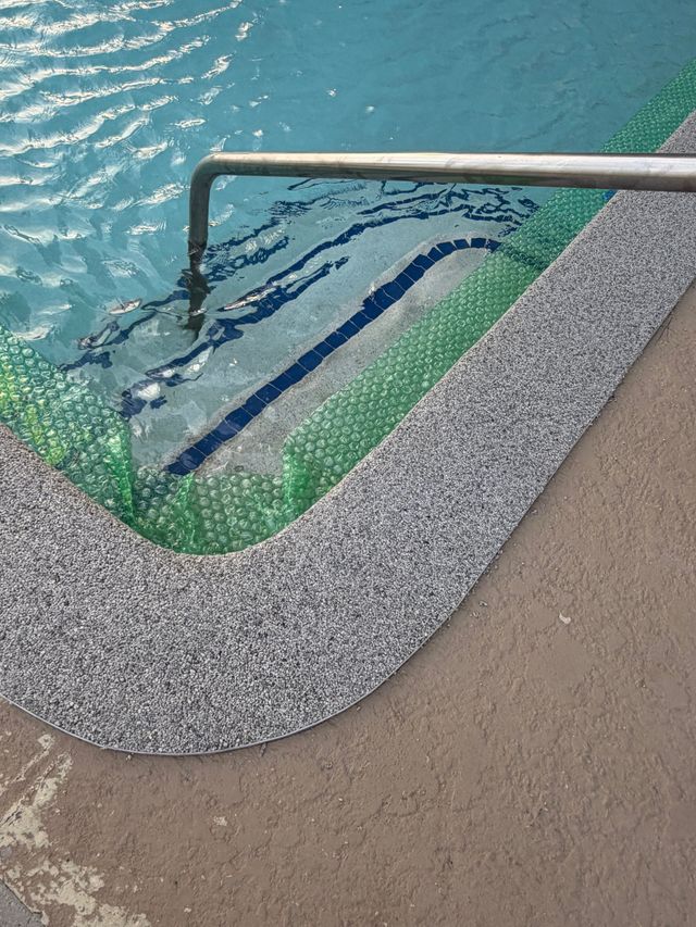 Swimming pool corner with metal handrail and turquoise water beside a pebble-textured deck