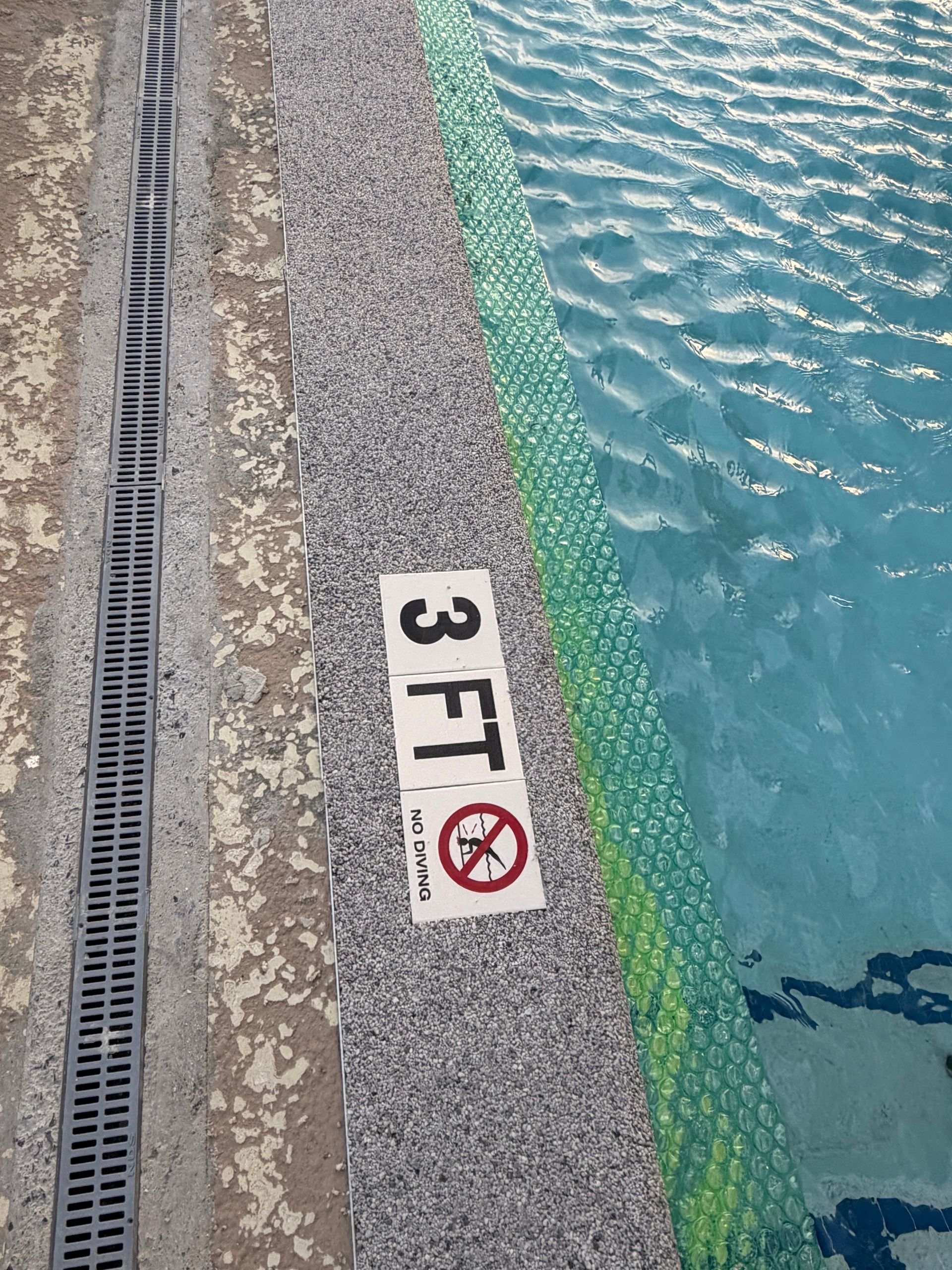 Pool edge marked “3 FT” beside a drain grate and blue water with a green lane line.