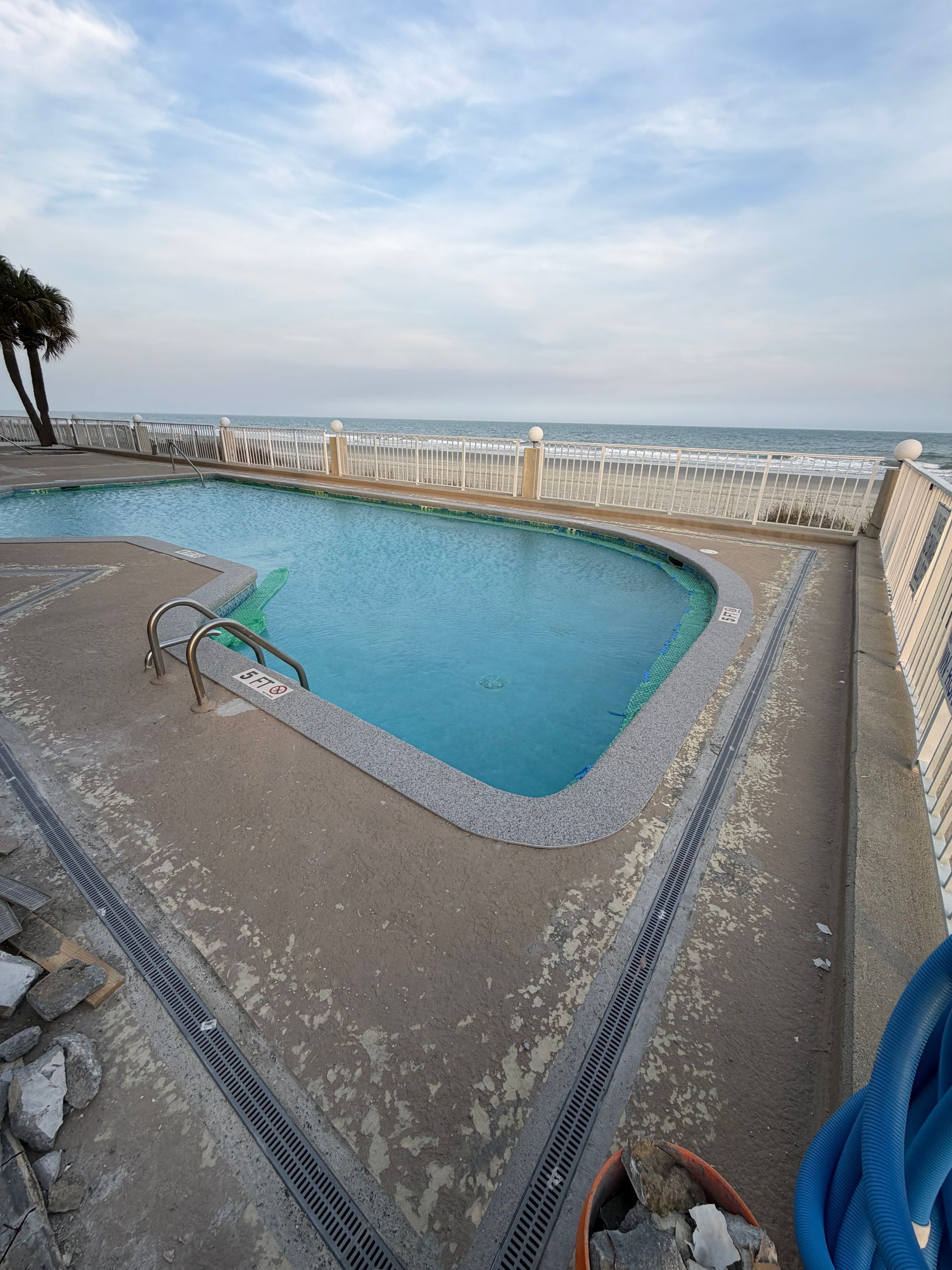 Outdoor pool with ocean view, blue water, white railings, and a cloudy sky.