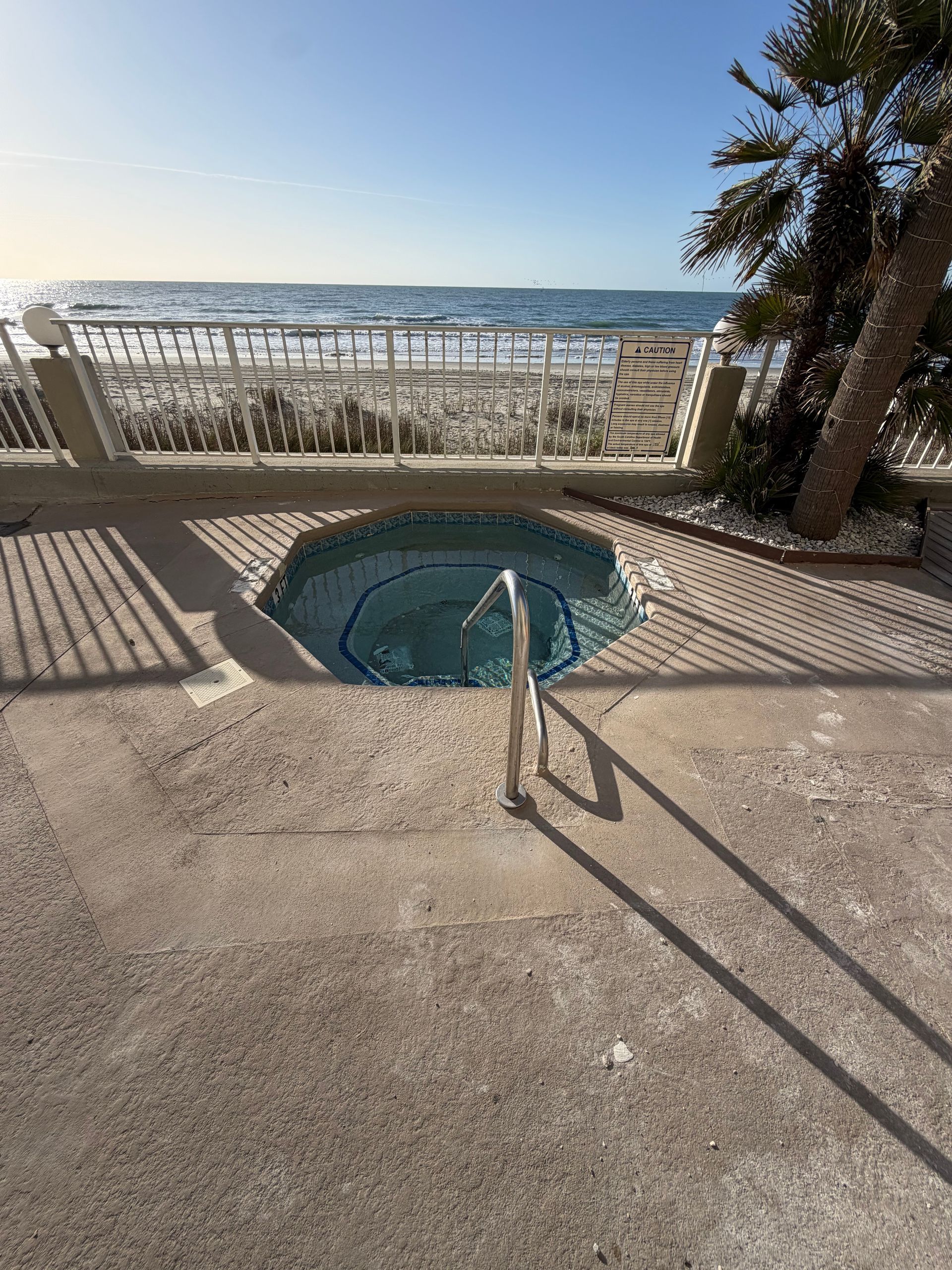 Hot tub beside a sunny beach promenade, with ocean view and long shadows at sunset