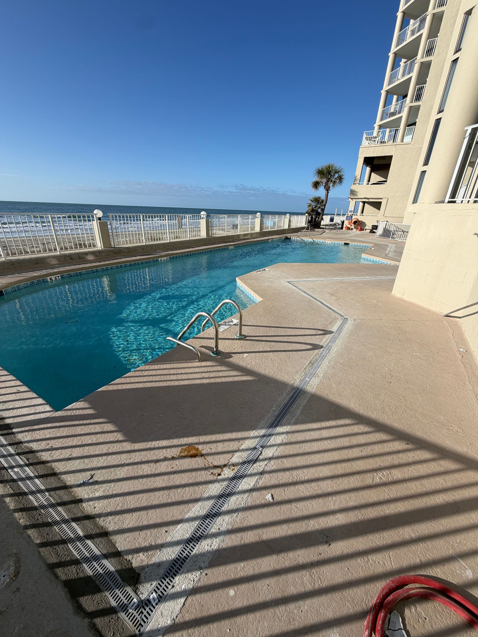 Rooftop pool with turquoise water, city and ocean views, and lounge chairs in bright sunlight