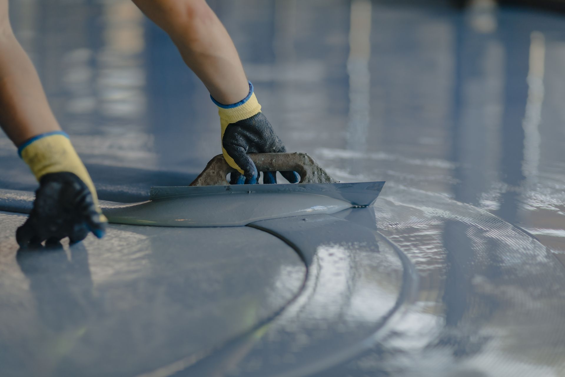 Gloved hands smoothing gray material on a glossy floor surface
