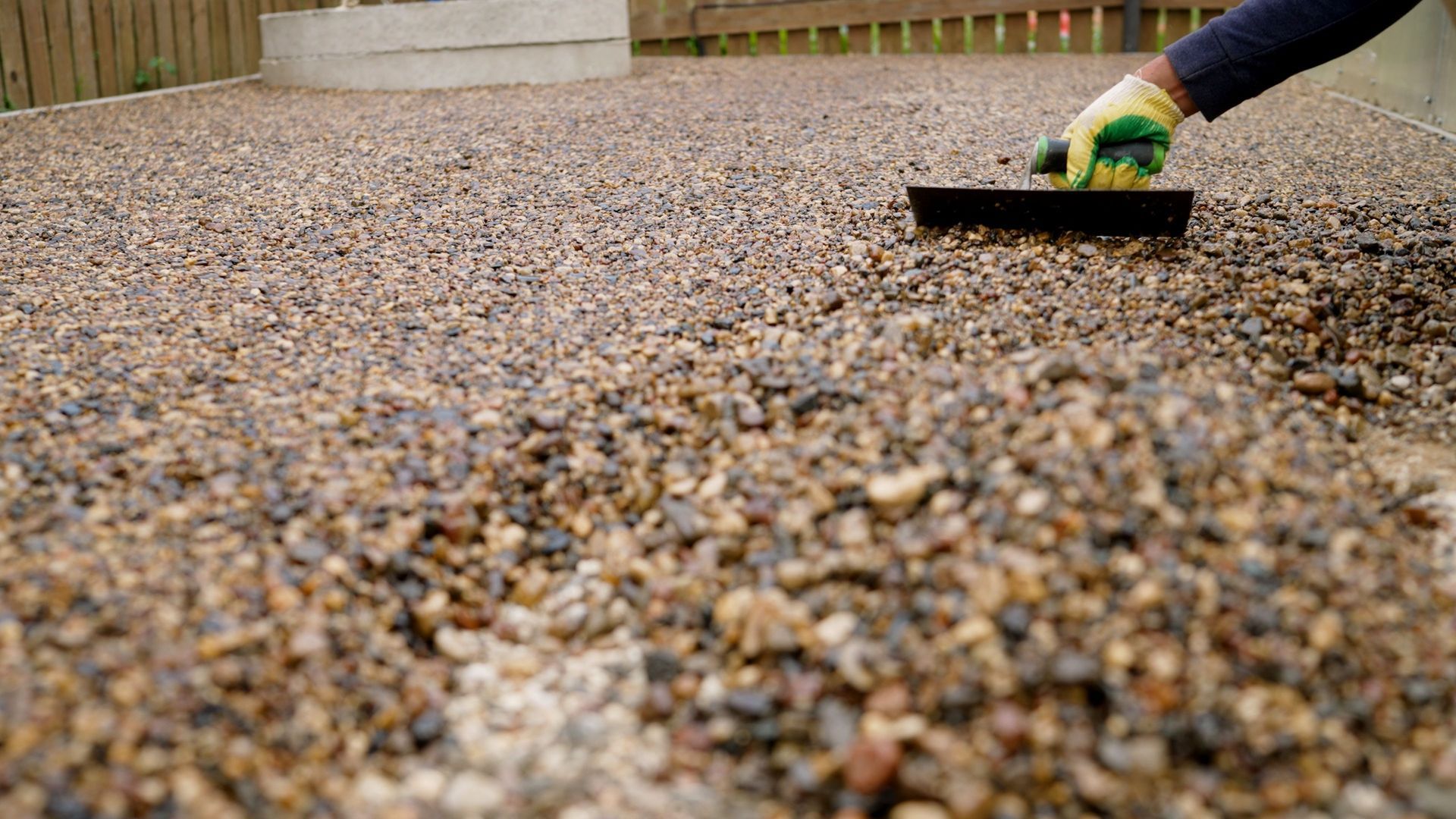 Hand leveling gravel in a yard with a black hand tool and green glove