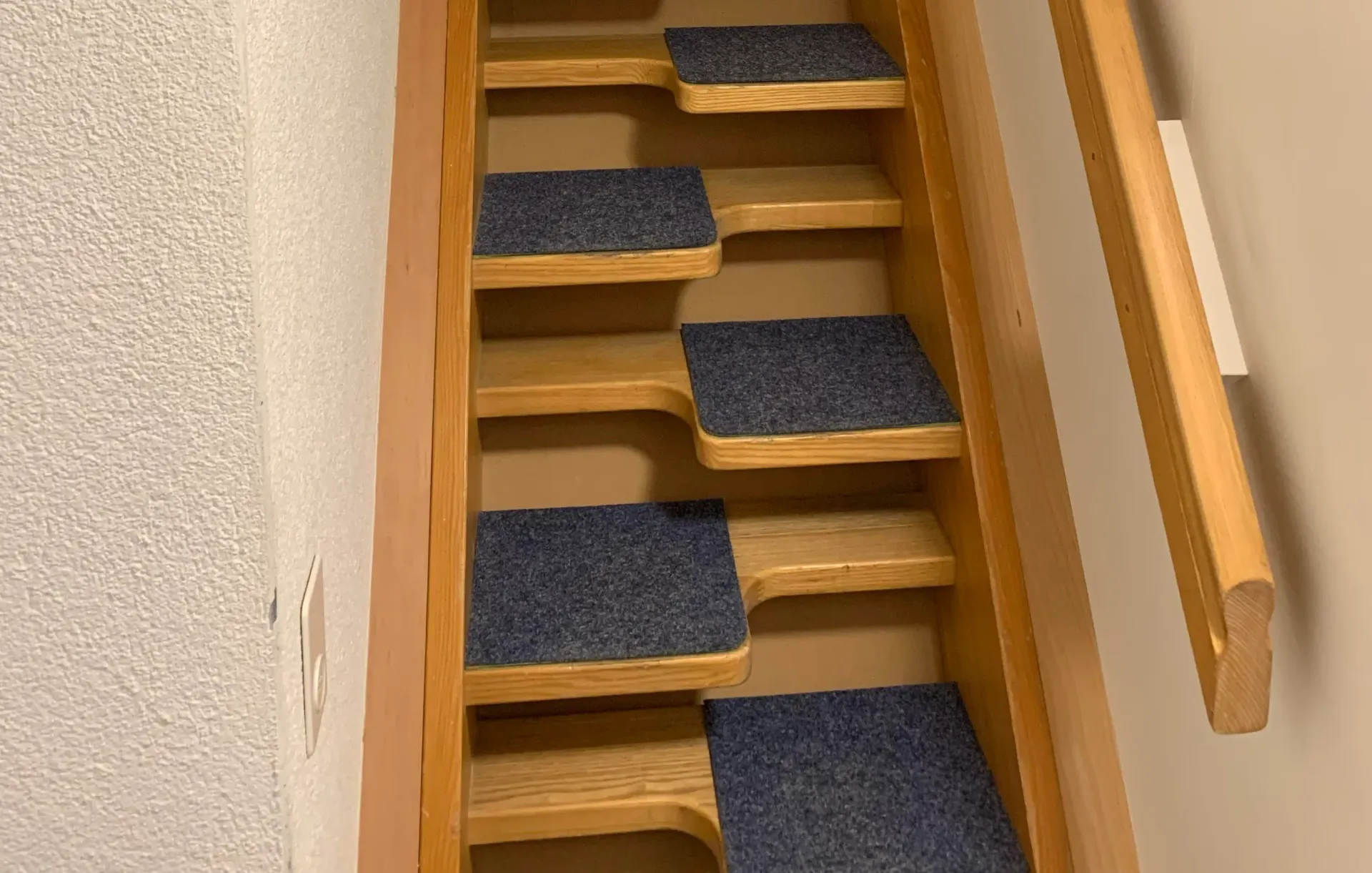 A wooden staircase with blue carpeted steps and a wooden railing.