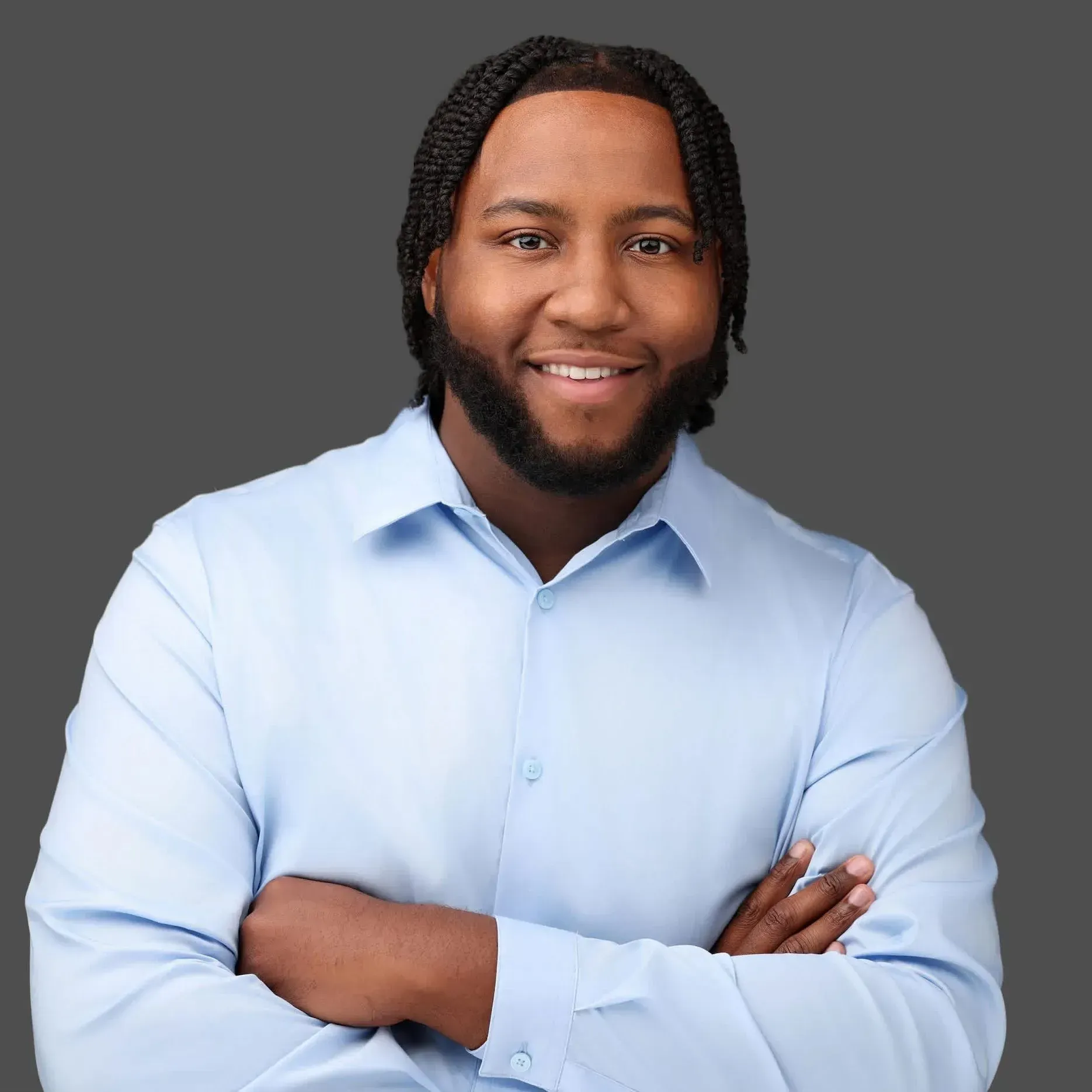 Smiling person in a light blue shirt with arms crossed against a gray background