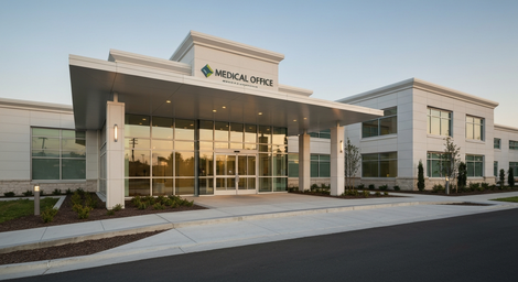 Modern medical clinic building exterior with glass entrance, columns, and landscaped front drive at sunset