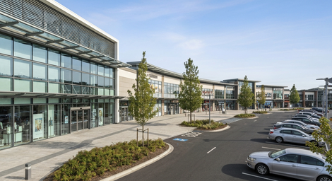 Modern office complex with glass facade, landscaped driveway, and parked cars under a clear sky