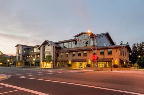 Modern multi-story building at dusk with lit windows and a red traffic light at a street corner
