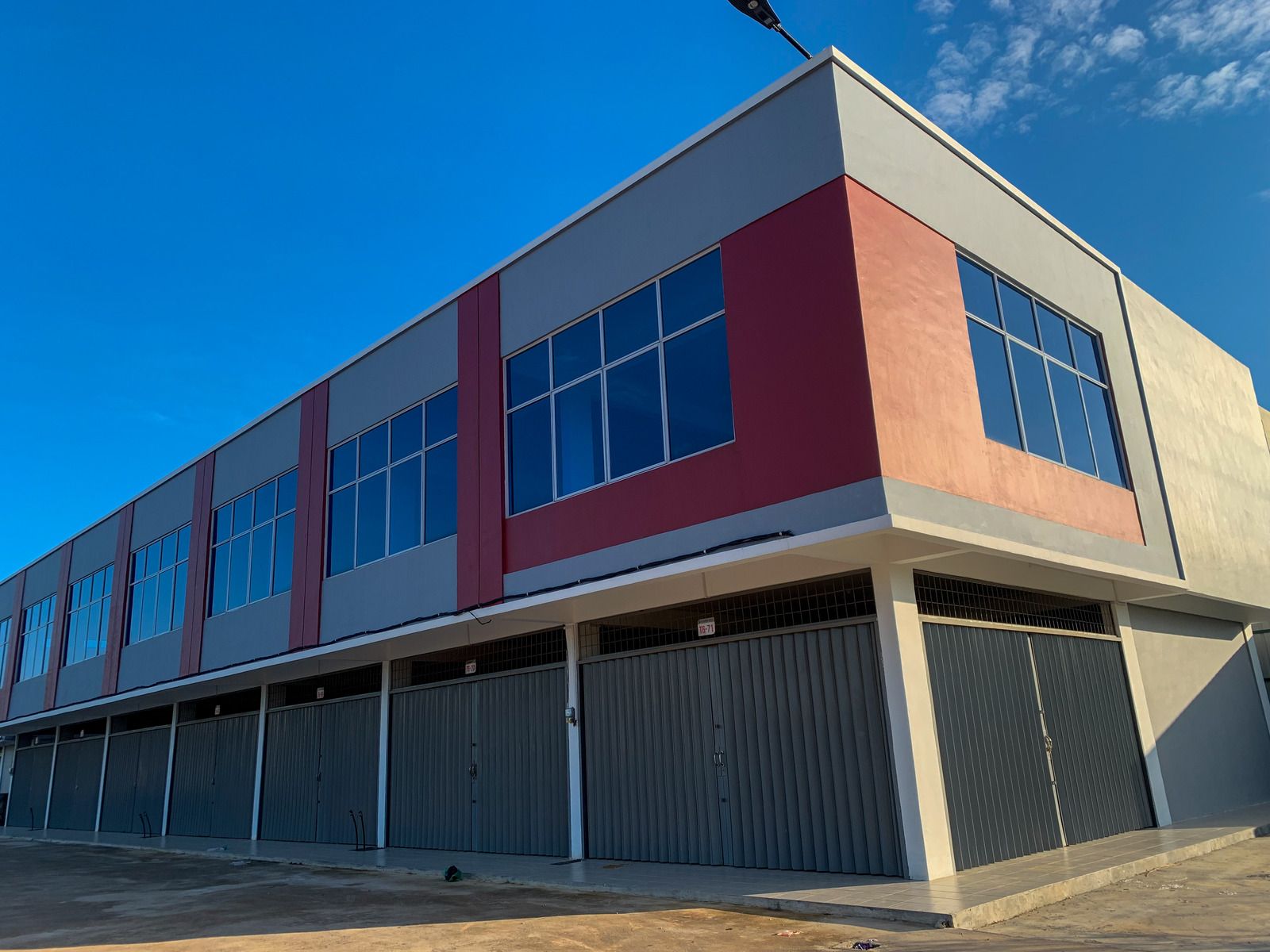 Modern two-story commercial building with red and beige facade, blue windows, and covered walkway under a clear sky