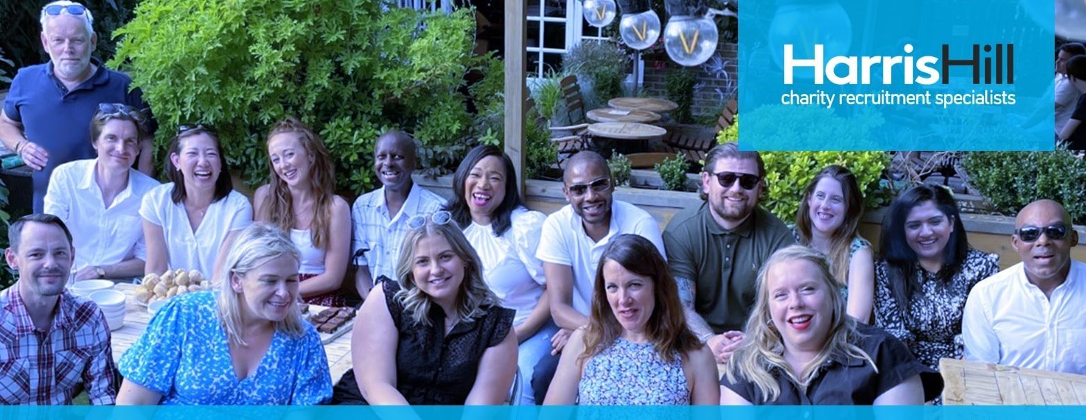 Group of people smiling, posing outdoors. Harris Hill logo in top right. Blue and green tones.
