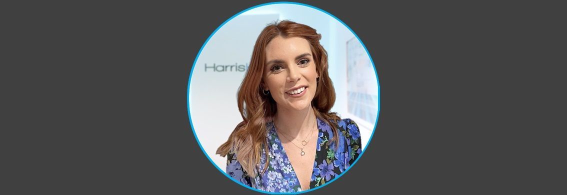 Woman with red hair, smiling, in a blue floral top, inside a light blue circle on a dark gray background.