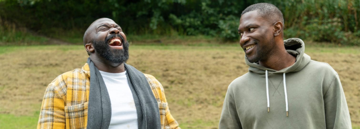 Two people laughing outside. One wears a plaid shirt, the other a green hoodie.