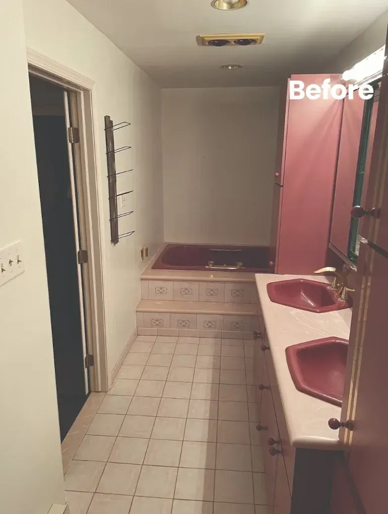 A long, narrow bathroom with red sinks and tub. Beige tile floor and stairs lead to the tub.