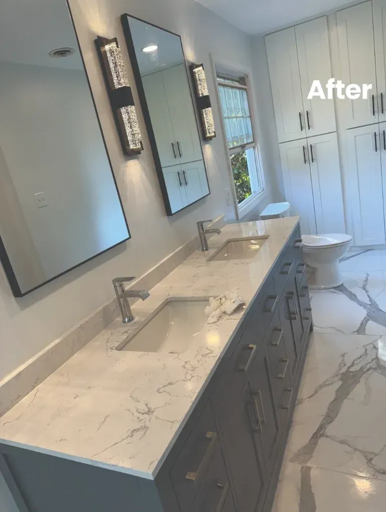 Modern bathroom with double vanity, marble countertops, mirrors, and white cabinets.