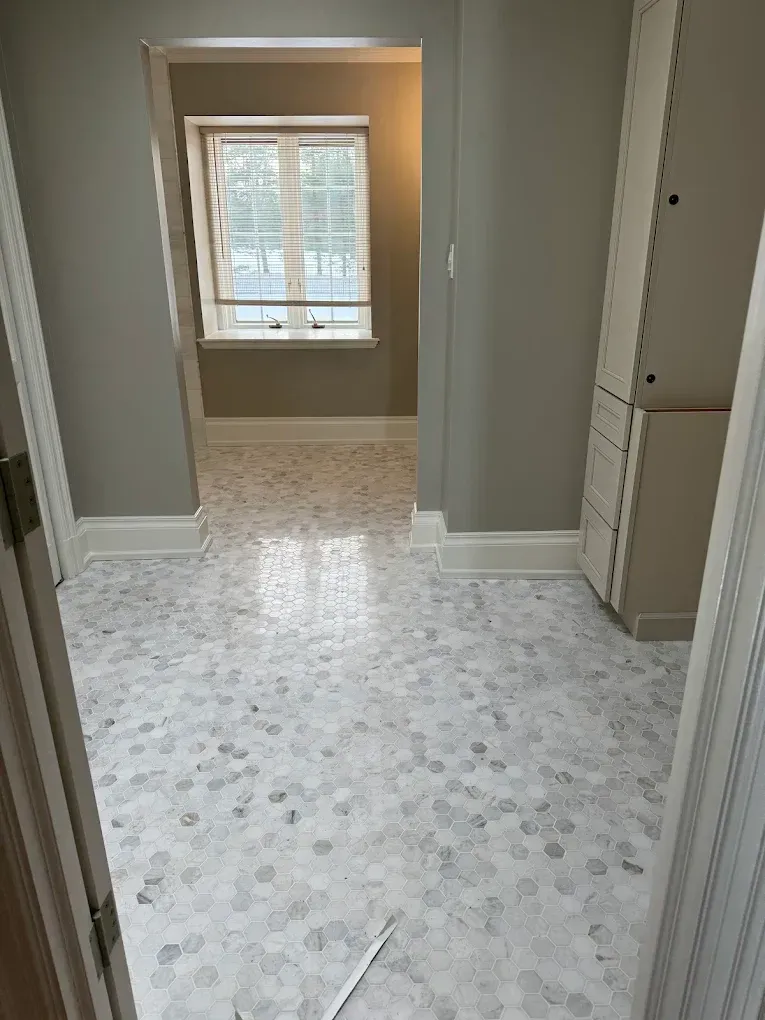 Hallway with light gray walls, patterned tile floor, and a window at the end.