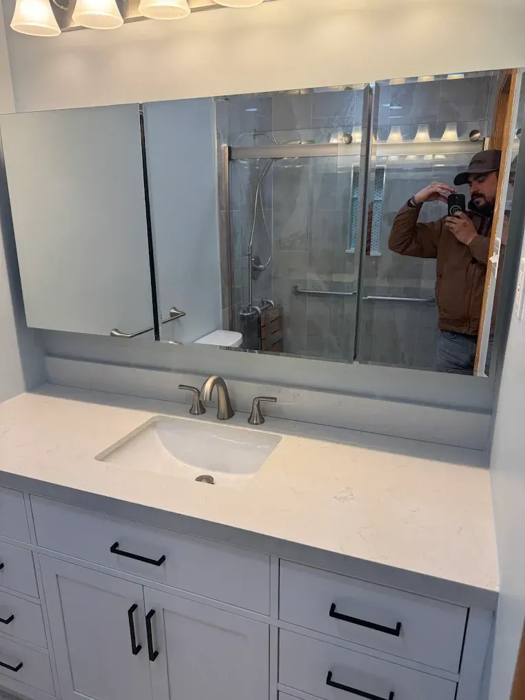 Bathroom with white vanity, sink, mirror, and a person taking a photo in the mirror.