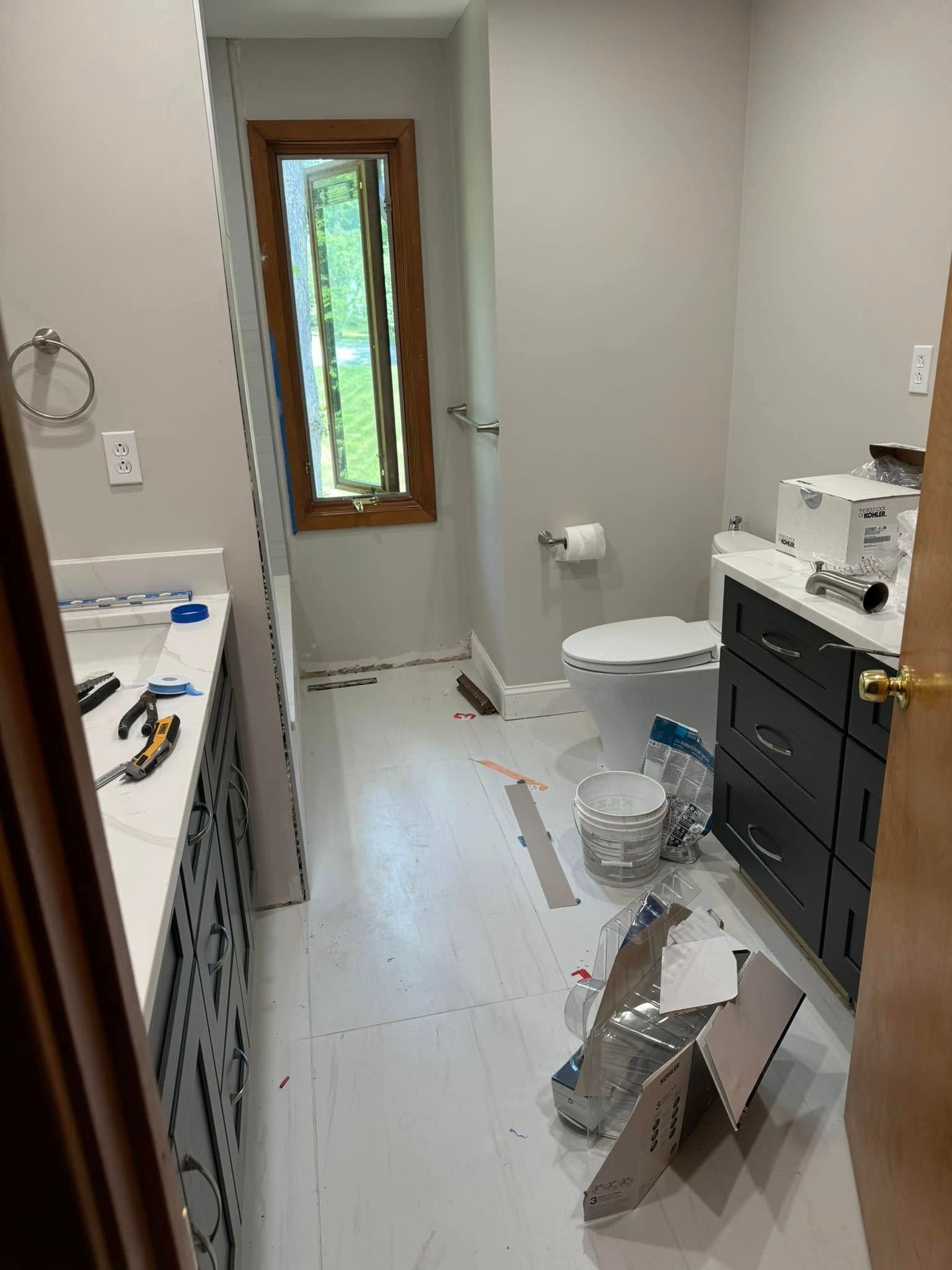 Bathroom under renovation with open window, toilet, vanity, and tools on the floor.