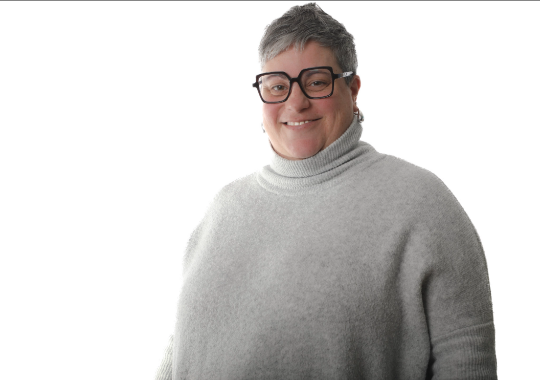 Personne souriante portant un pull à col roulé gris et des lunettes sur fond blanc