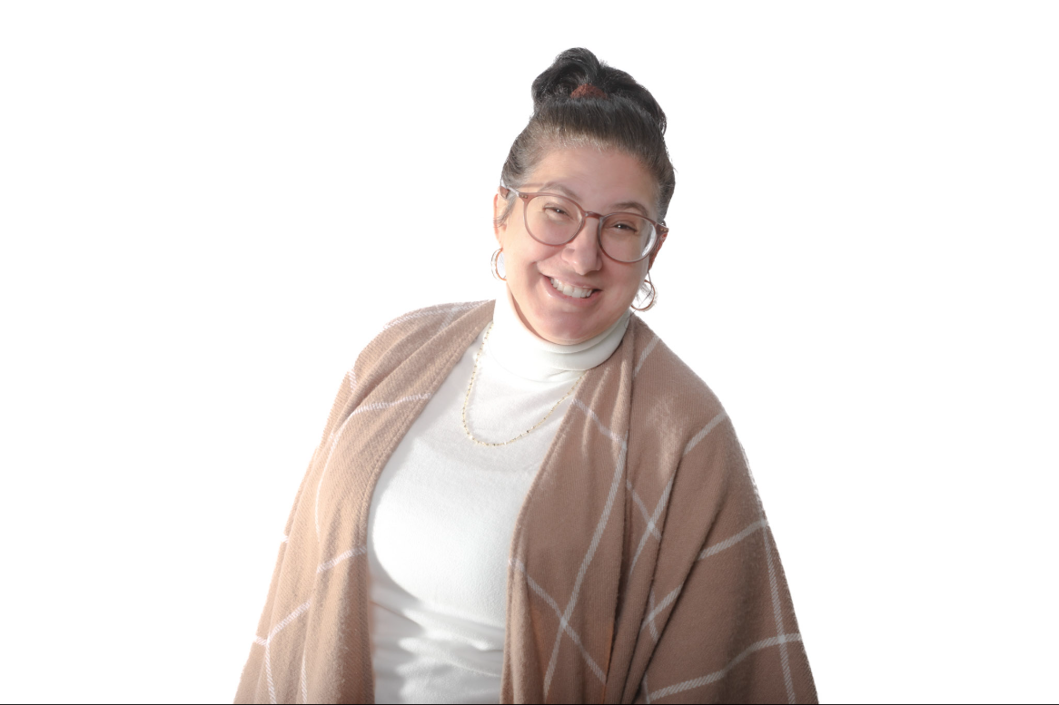 Personne souriante portant des lunettes et un châle beige sur un col roulé blanc, sur fond blanc.
