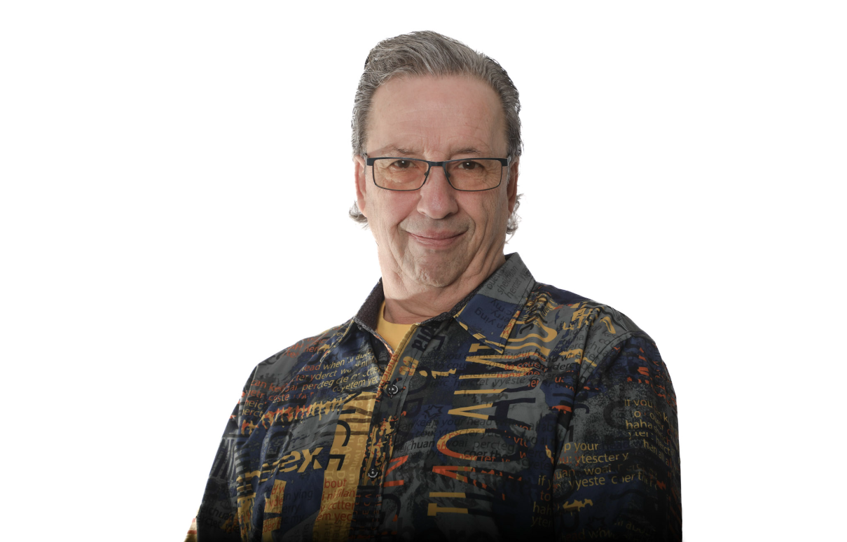 Homme souriant portant des lunettes et une chemise à motifs foncés sur fond blanc