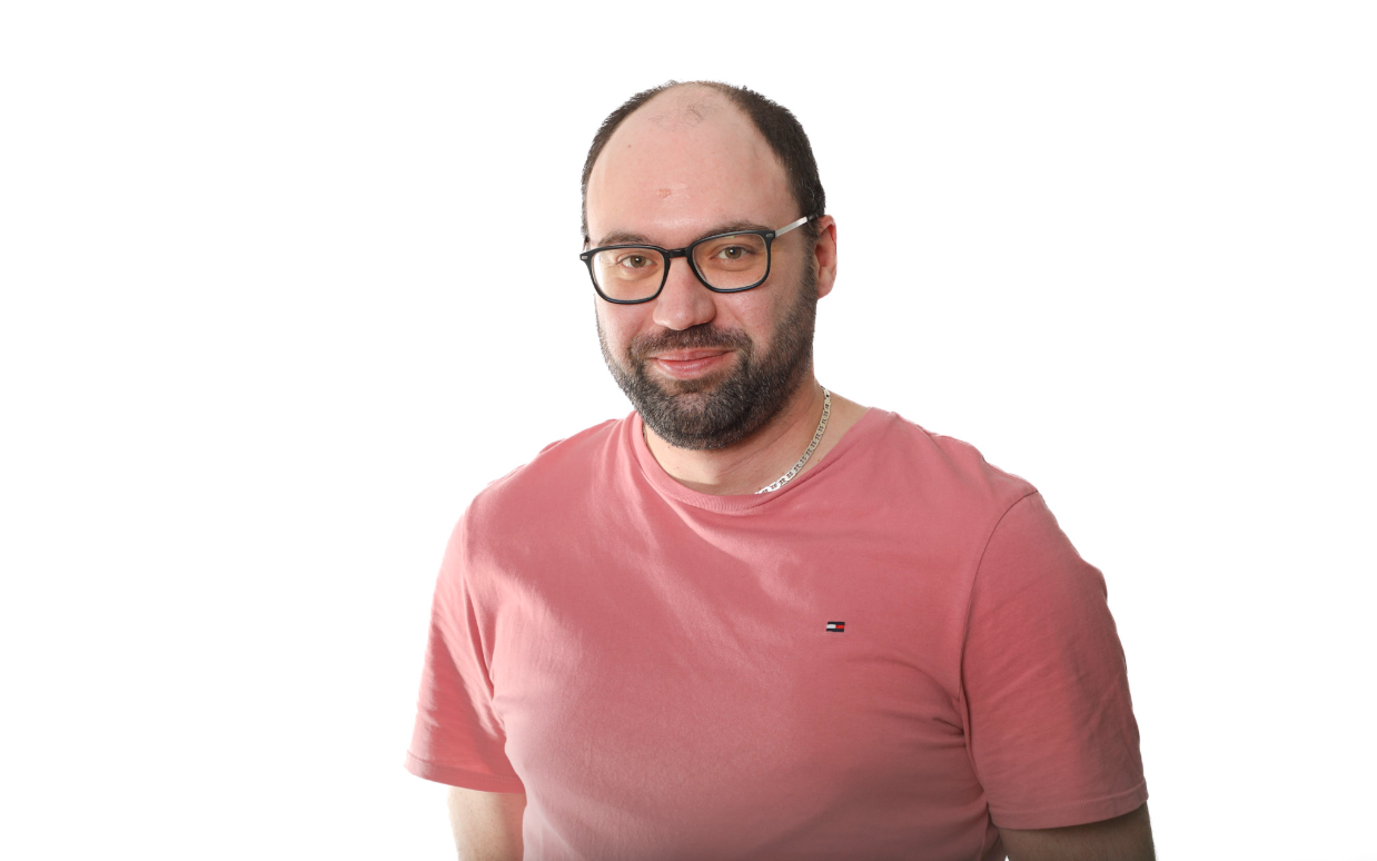 Un homme en t-shirt rose et lunettes sourit sur fond blanc