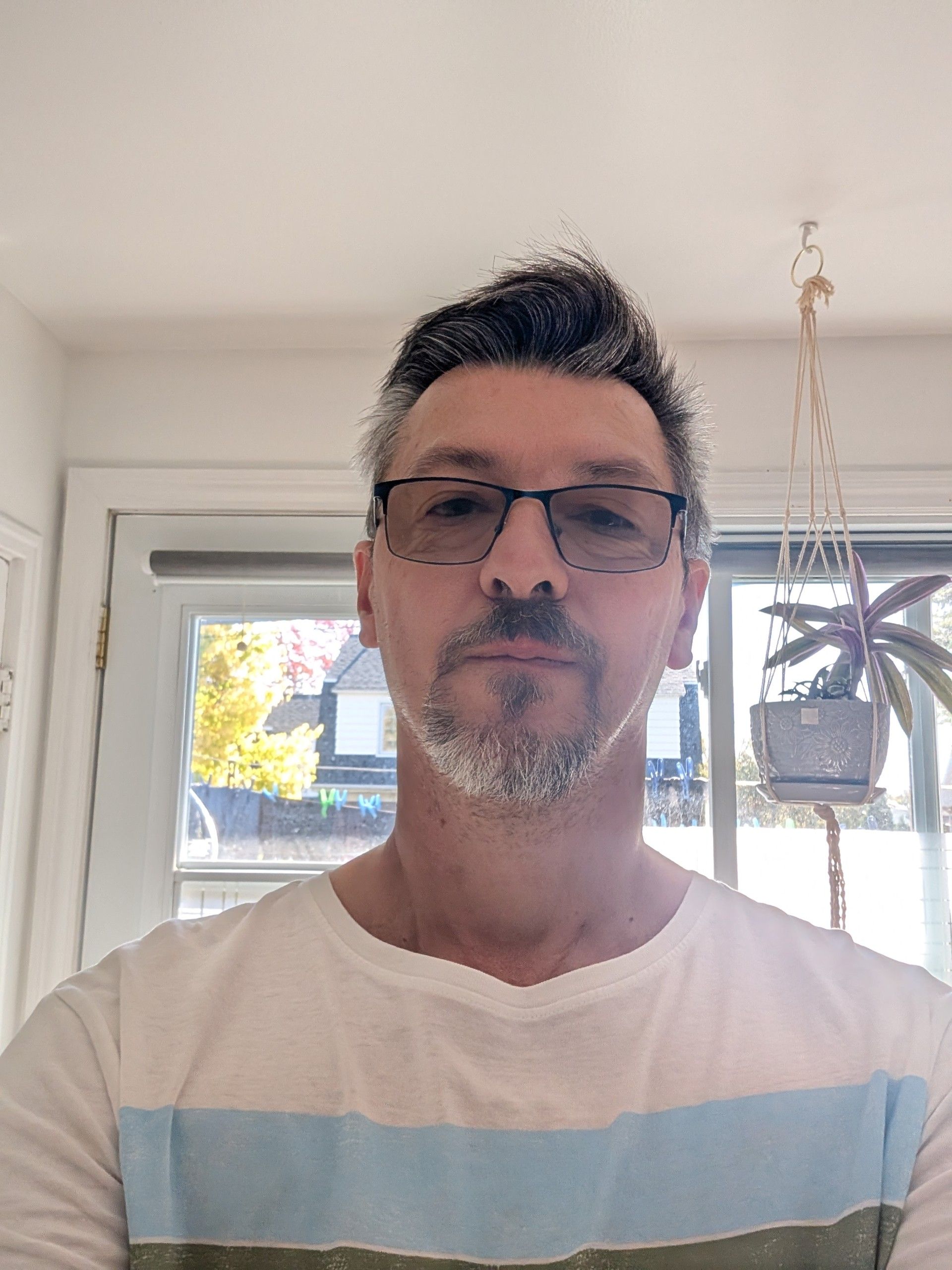 Un homme portant des lunettes et une chemise à rayures blanches se tient à l'intérieur, devant une fenêtre.