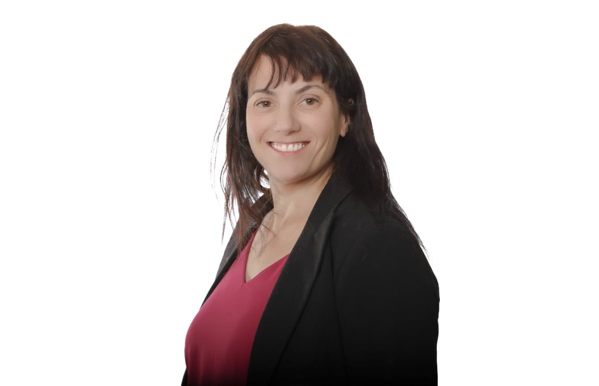 Personne souriante portant un blazer noir sur un haut magenta sur fond blanc