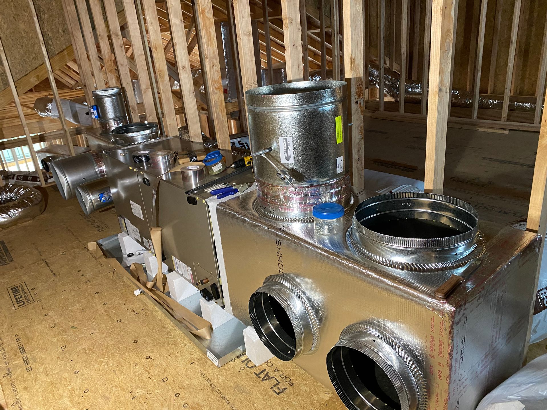 HVAC system installation in an attic, featuring metallic ducts and vents, wood framing visible.