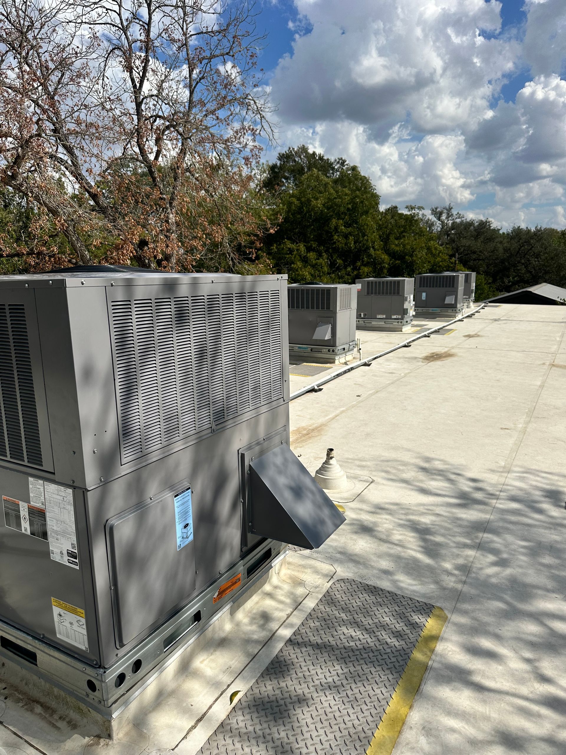 AC units on a rooftop under a partly cloudy sky; trees in the background.