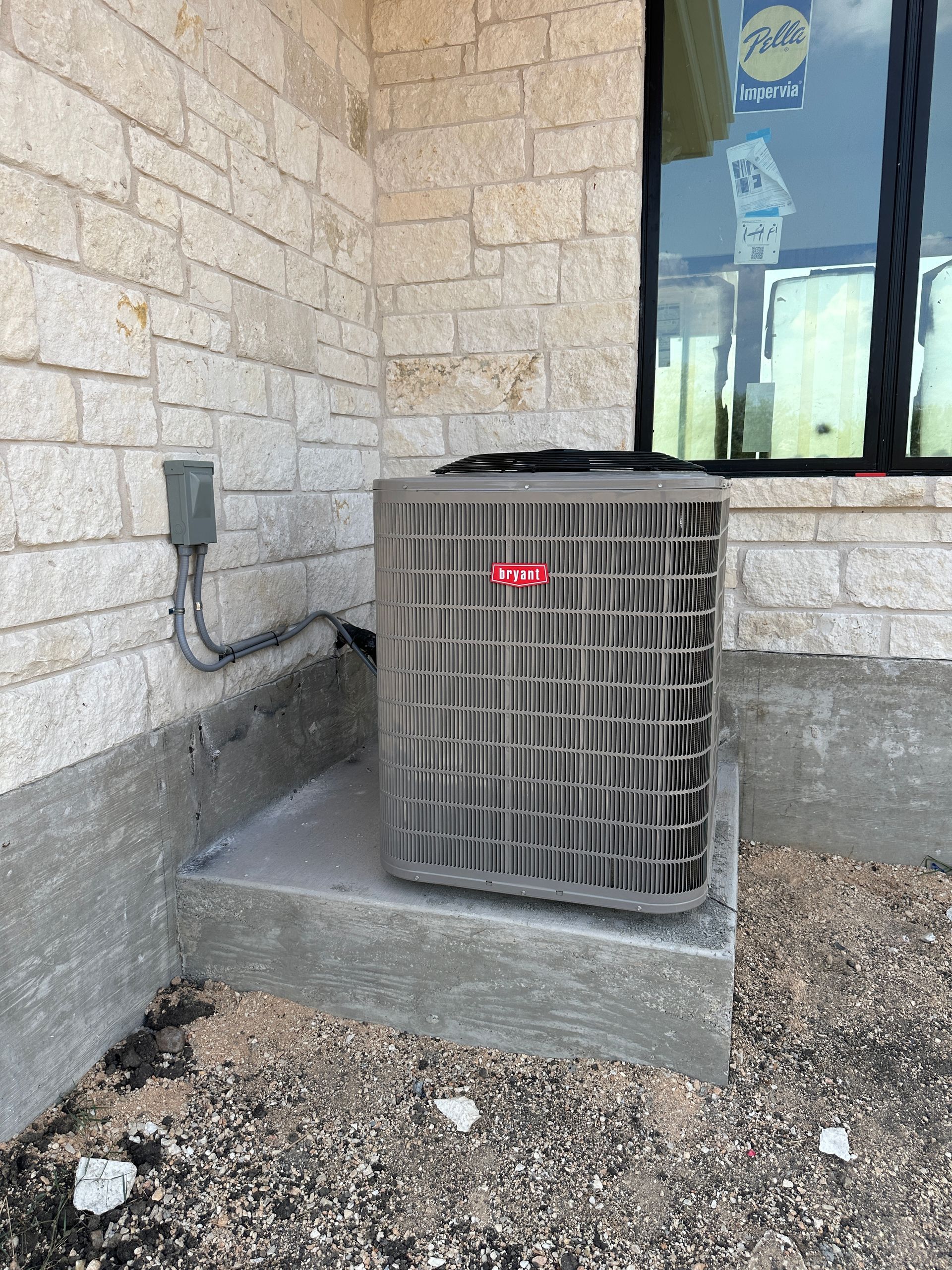 Air conditioning unit outside a building with stone siding and a window.
