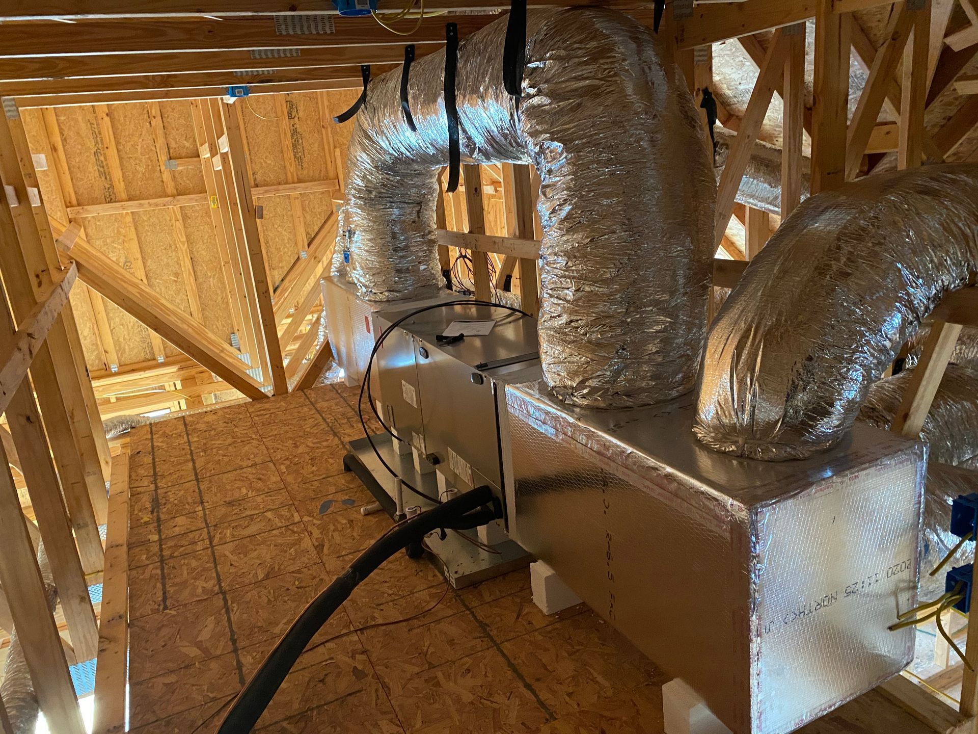 HVAC unit installed in attic with ductwork, set among wooden beams and boards.