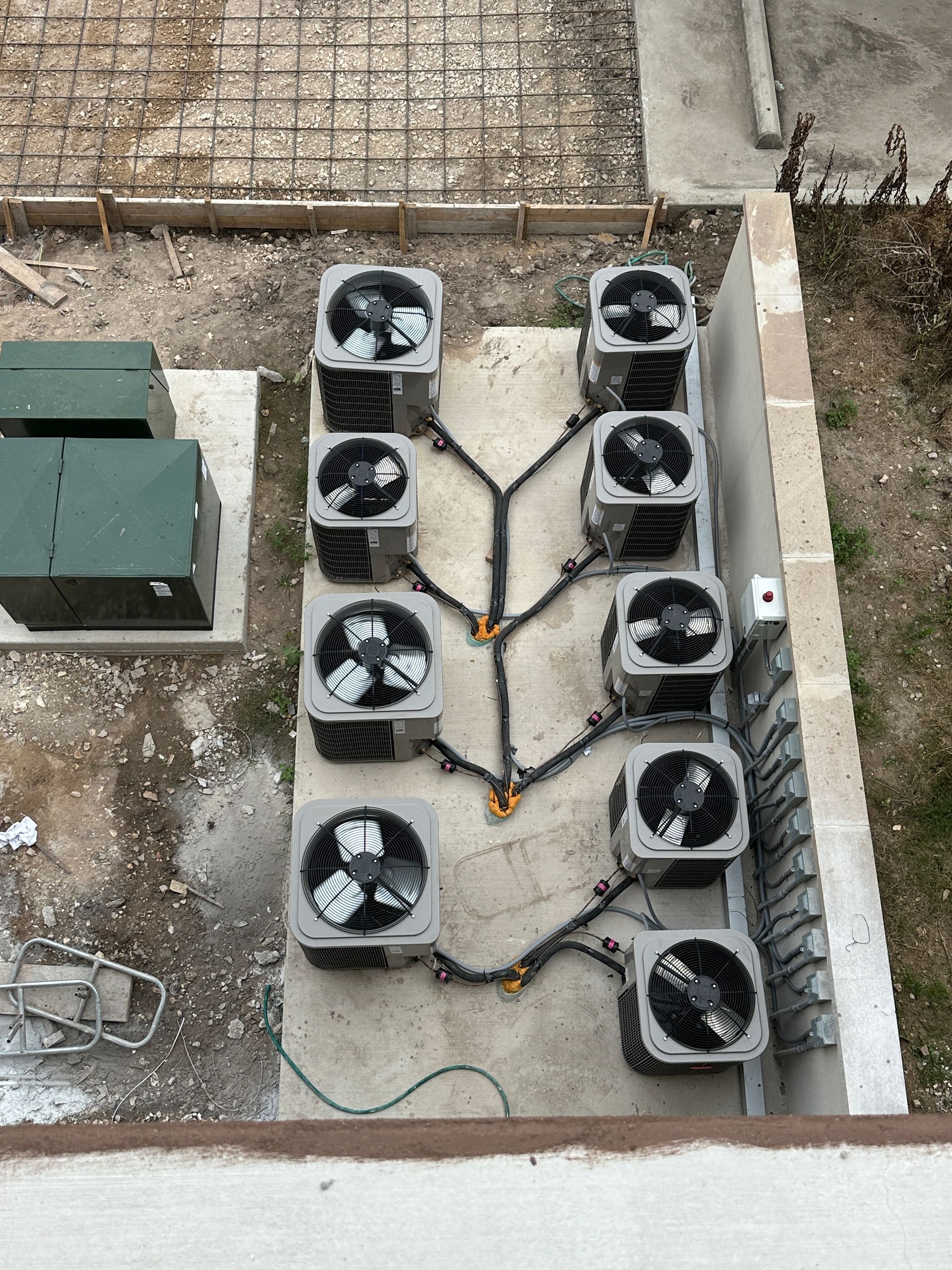 Overhead view of several air conditioning units connected by pipes on a concrete pad outdoors.