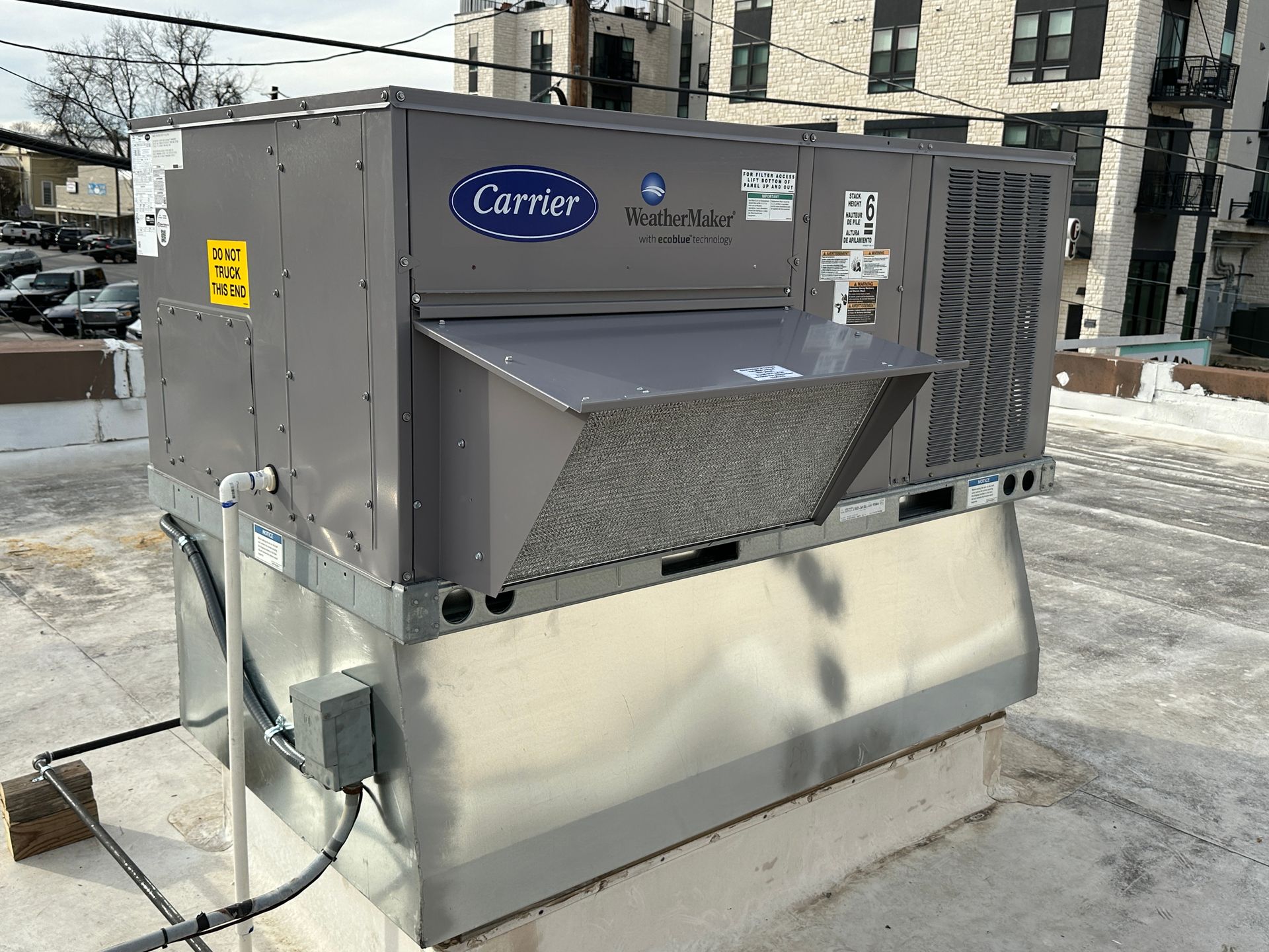 Carrier rooftop HVAC unit on a building roof. Gray, silver, with warning labels.