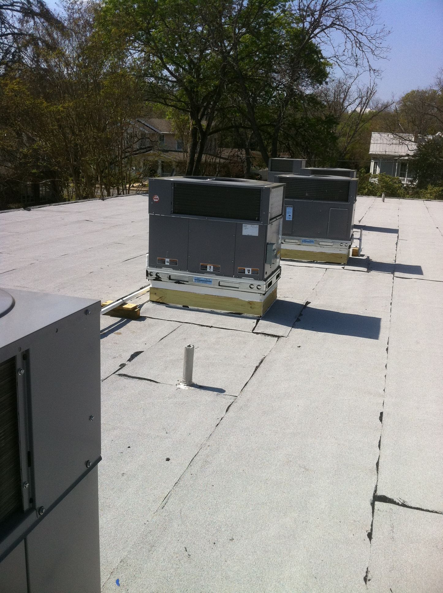 HVAC units on a flat rooftop. Gray units with yellow insulation, next to trees and a small building.
