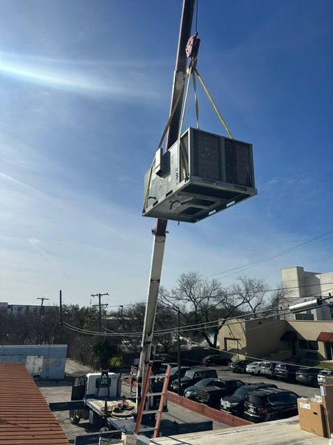 A crane lifting an HVAC unit onto a rooftop on a sunny day.