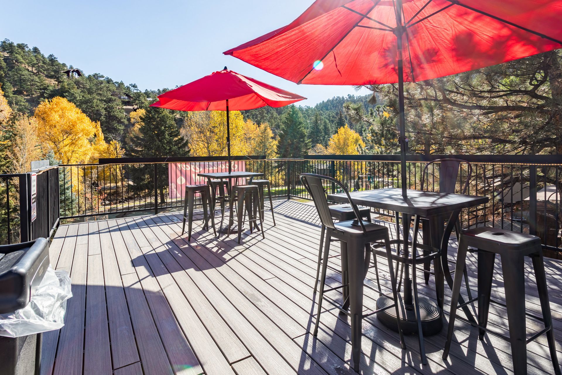 A wooden deck with tables and chairs and red umbrellas.