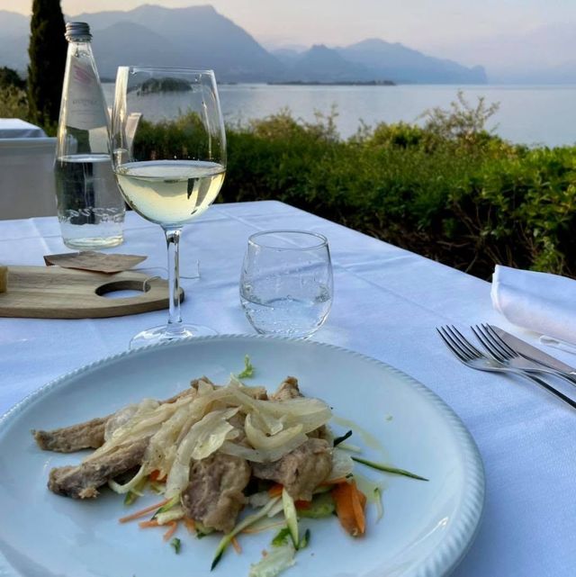 Vino e pesce servito su un tavolo in riva al mare al tramonto, con le montagne sullo sfondo.