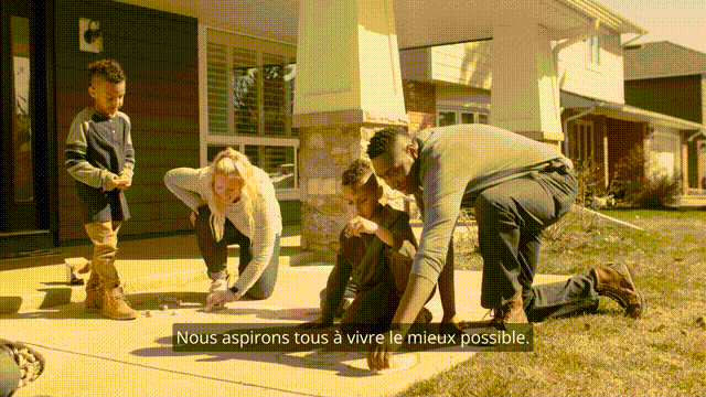 A family is kneeling on the ground in front of a house from a Sun Life video