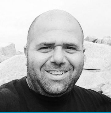 A bald man with a beard is smiling in a black and white photo.