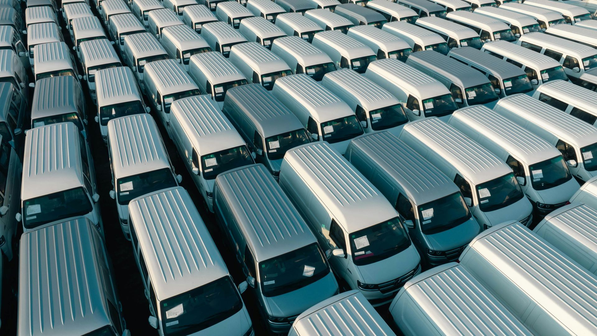 Rows of silver buses packed tightly in a parking lot, viewed from above.