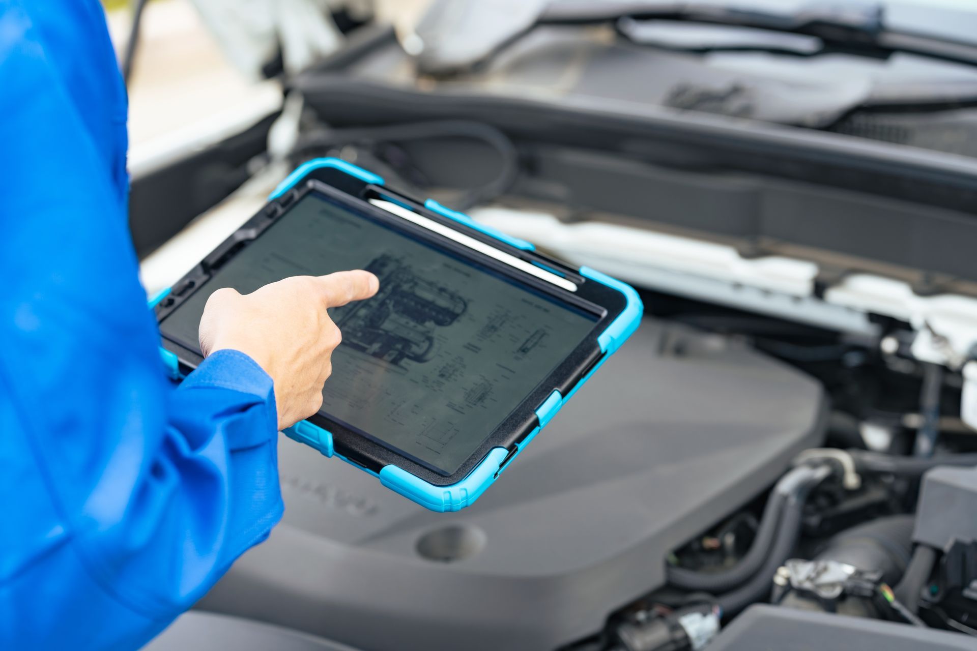Person using a tablet to inspect a car engine under the hood