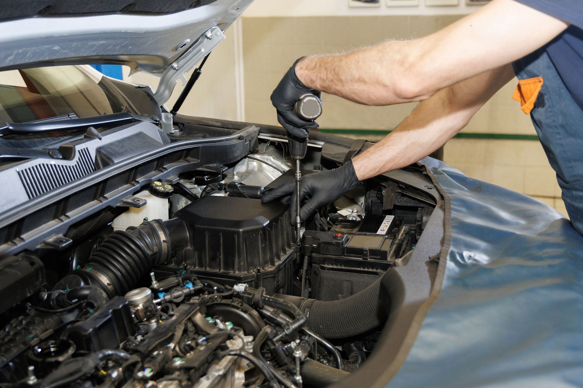 Mechanic working under an open car hood, adjusting engine components with gloved hands