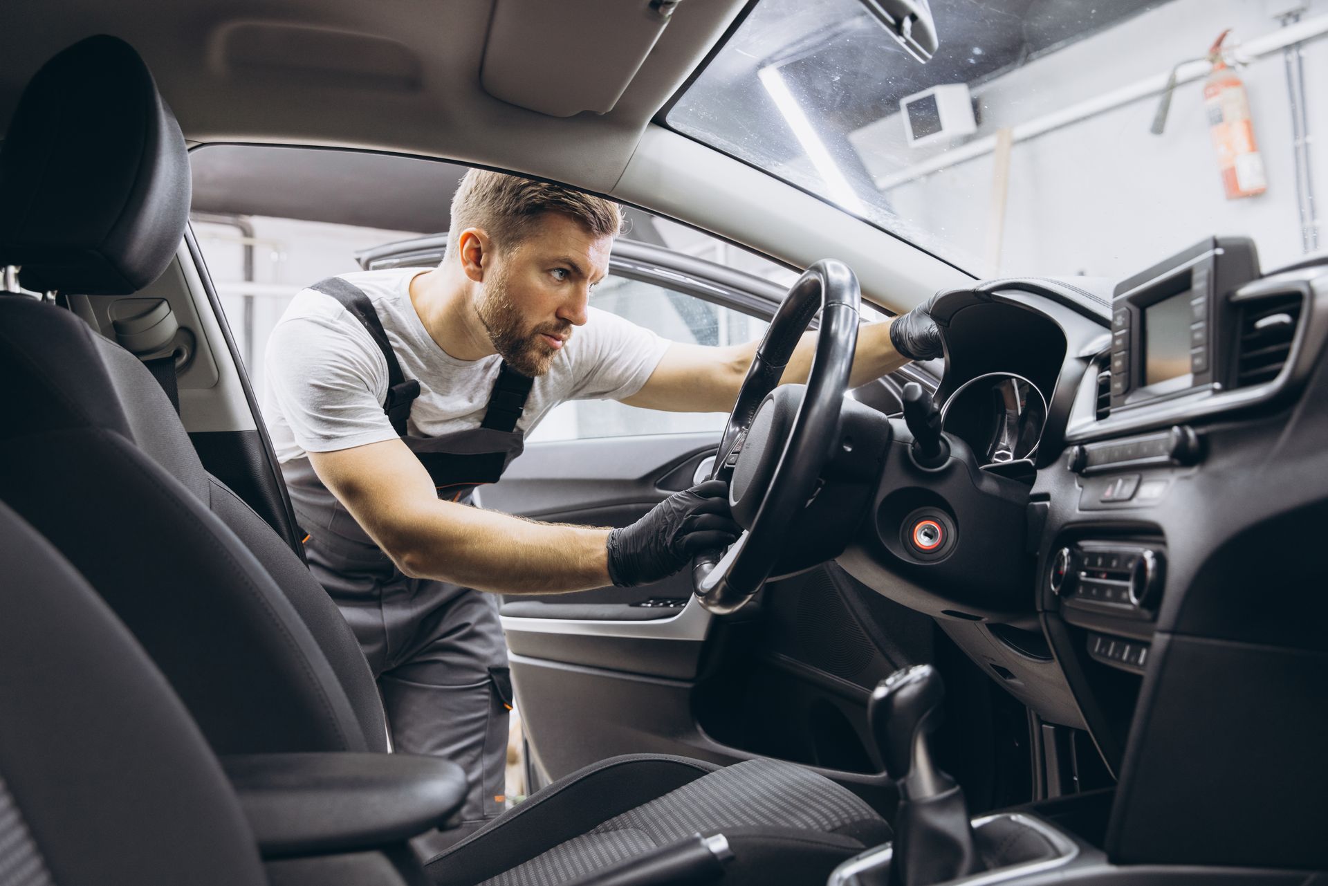 Man leaning into a car interior, reaching toward the steering wheel and dashboard for maintenance or cleaning
