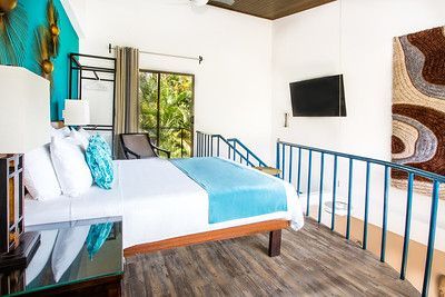 Modern bedroom with blue accents, white bed, wall-mounted TV, and balcony view through open curtains