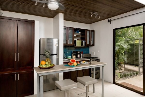 Modern kitchen with dark wood cabinets, island table, fruit, and open doorway to a garden patio.