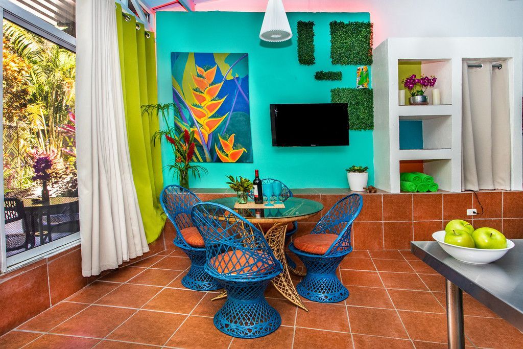 Bright living room with turquoise wall, blue wicker chairs, wall TV, and terracotta tile floor.